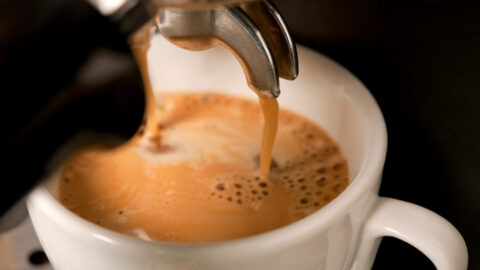 Close-up of fresh espresso pouring from a machine into a white ceramic cup, with a layer of crema forming on top.