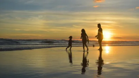 Family enjoying a beach walk at sunset, reflecting on calm waves, ideal for relaxation and seaside hotel stays.