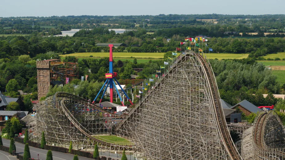 Thrilling wooden roller coaster and lush green landscape at theme park hotel, promising adventure and scenic views.