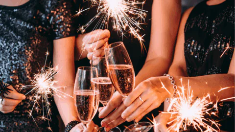 Three people holding sparklers and toasting with champagne glasses, dressed in festive attire.