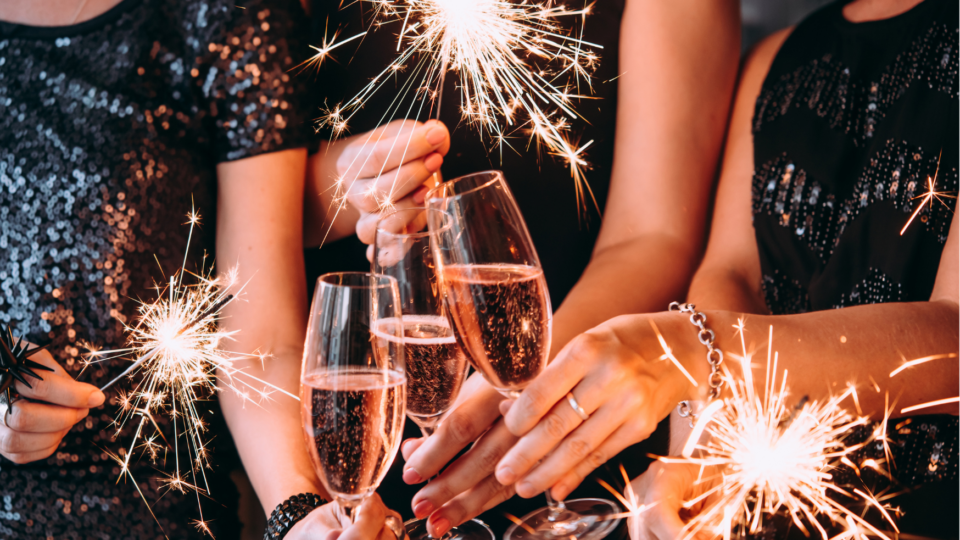 Three people holding sparklers and toasting with champagne glasses, dressed in festive attire.