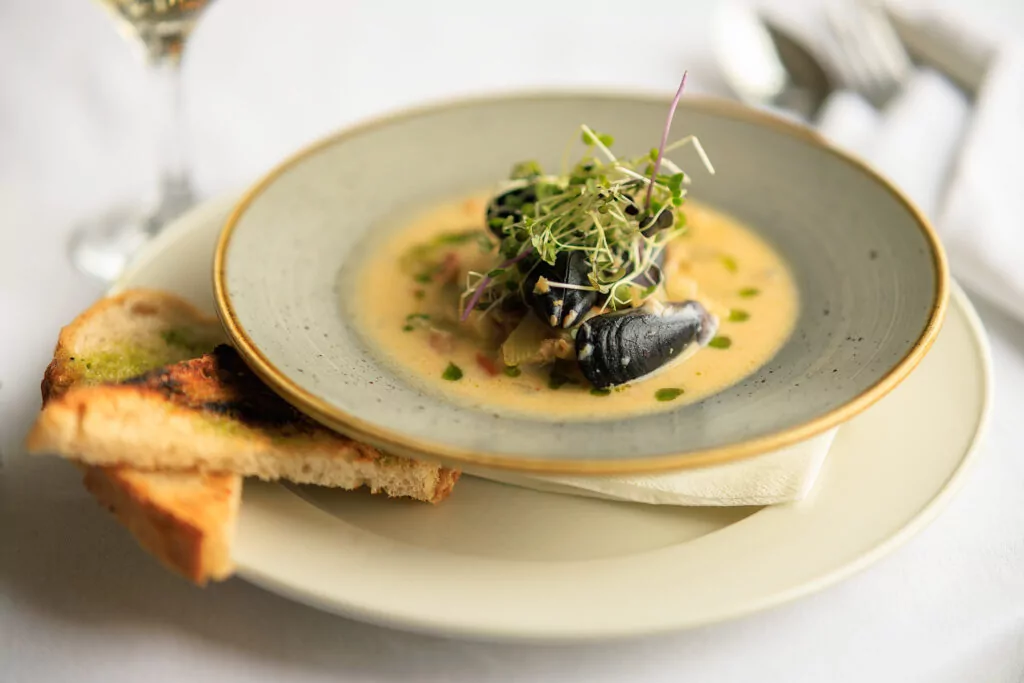 Seafood showder in a bowl showing mussels and watercress garnish. on a plate with toast