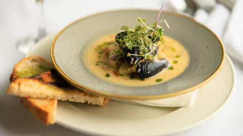 Seafood showder in a bowl showing mussels and watercress garnish. on a plate with toast