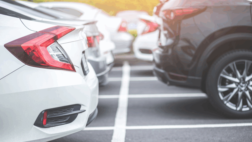 Close-up view of several parked cars in a parking lot, showing the rear ends and tail lights of white and black vehicles.
