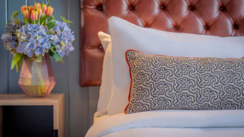 Cosy hotel room with plush, tufted headboard, elegant floral arrangement, and stylish decorative pillow on crisp white bedding.