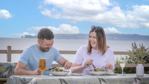 Guests dining outdoors with stunning ocean views, enjoying delicious meals and drinks at a beautifully set table.