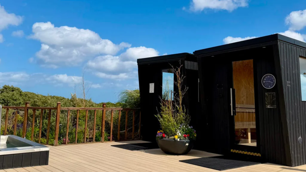 Relaxing outdoor sauna and hot tub on sunlit deck, surrounded by lush greenery and blue skies at luxury UK hotel.