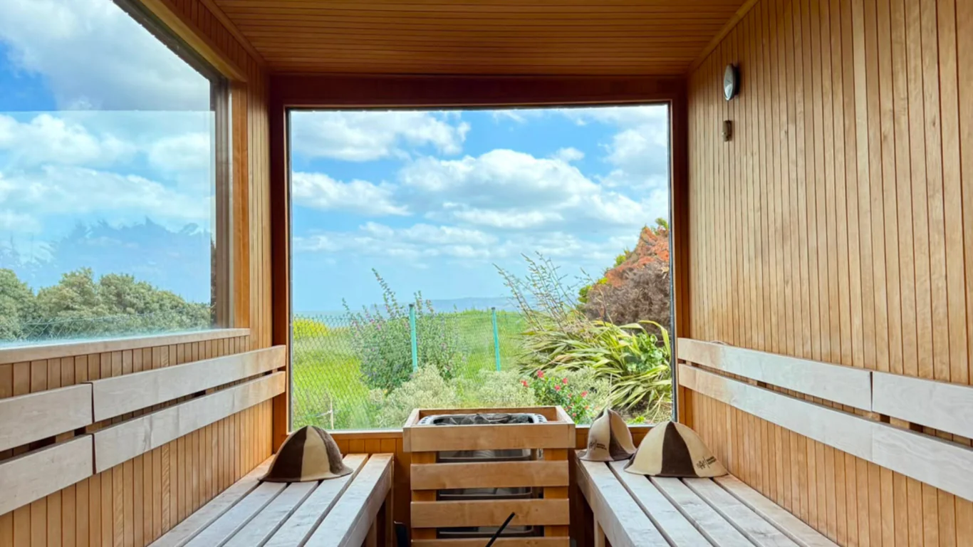 Relaxing wooden sauna with window views of lush green landscape and blue skies at luxurious hotel retreat.