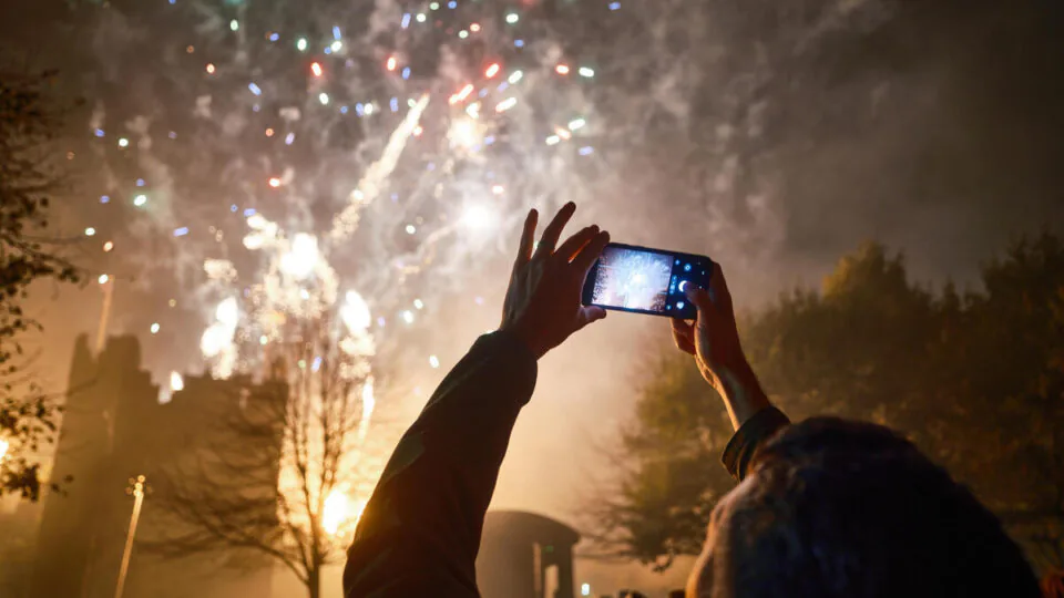Guests capturing vibrant fireworks over hotel gardens, surrounded by lush trees and a festive atmosphere.